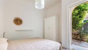 Un dormitorio con cama, un armario blanco, una lámpara colgante y vistas a zonas verdes.