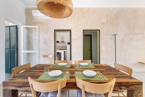Un coin repas avec une table en bois, dressée pour quatre personnes, entourée de chaises, et un luminaire tressé suspendu au-dessus.