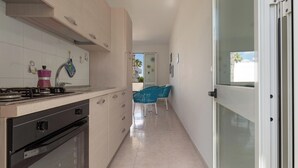 Eine schmale Küche mit Herd, Backofen und Schränken. Eine Tür führt zu einem Balkon mit Außenblick.