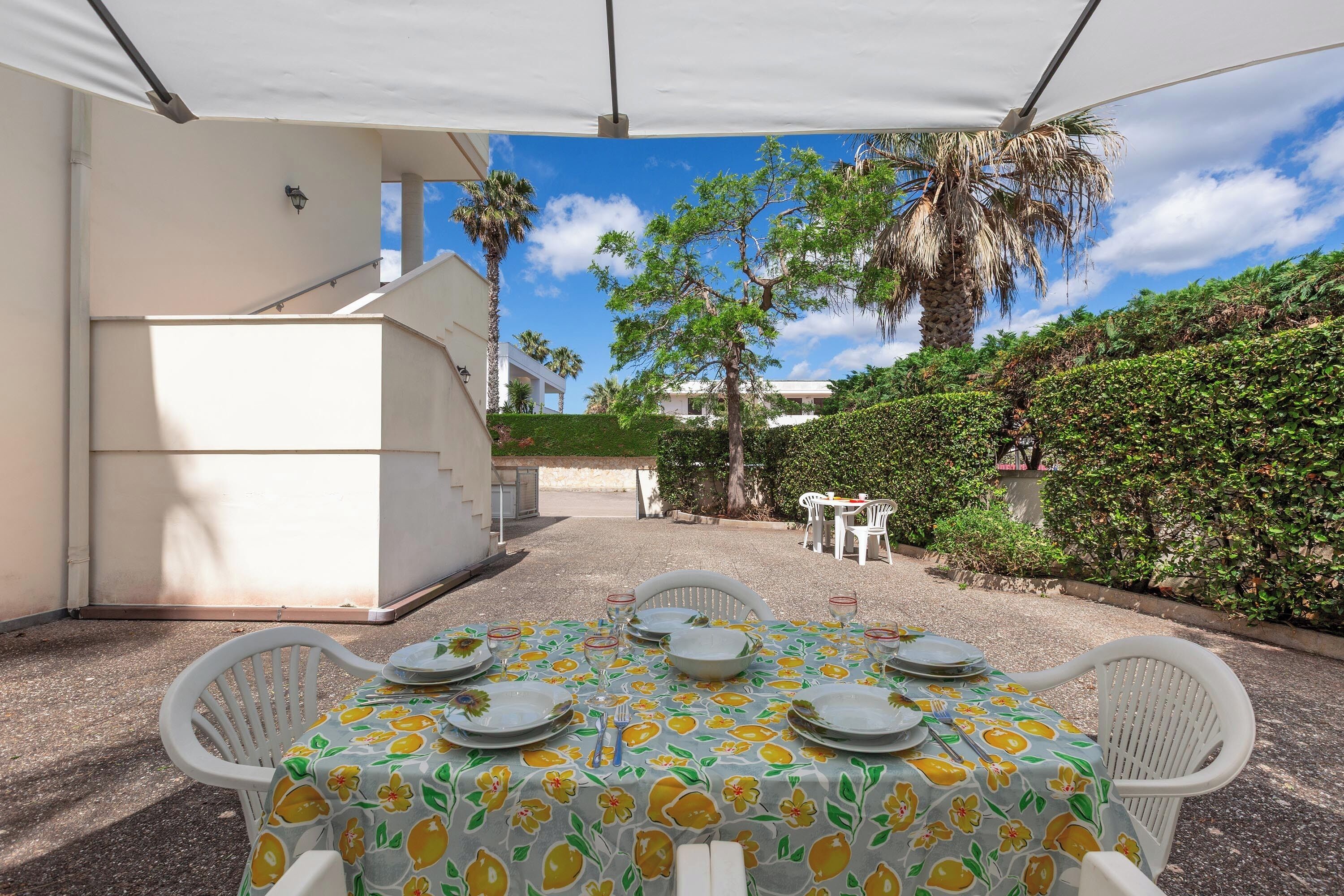 A covered outdoor dining area with a table set for four, surrounded by white chairs, under a white canopy.