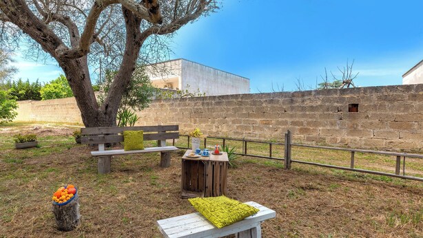 A rustic outdoor seating area with a wooden bench and a small table, surrounded by a stone wall and a tree. - Casina Gigina by BarbarHouse (Torre Specchia Ruggeri)