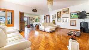 A spacious living room with a large sofa, a dining area with a table and chairs, and a television on a stand. - Villa di Carmen by BarbarHouse (Castrignano del Capo)
