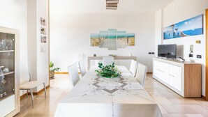 A modern dining area with a long table, white chairs, a central plant, and a painting above. - Villa di Carmen by BarbarHouse (Castrignano del Capo)