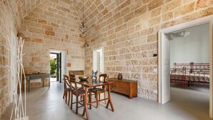 Une pièce spacieuse avec un plafond haut et des murs en briques apparentes, comprenant un coin repas avec des meubles en bois et une vue sur l’extérieur.