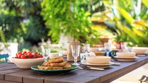 Une table en bois, dressée avec des assiettes, des bols et des verres, entourée d’une végétation luxuriante.