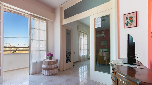 A spacious room with a balcony, a small round table with a vase, and a television on a wooden cabinet. - Nando`s Bellavista House By BarbarHouse (Porto Cesareo)