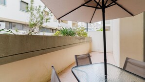Taula de vidre amb cadires i un para-sol gran en una zona de terrassa a l'aire lliure.