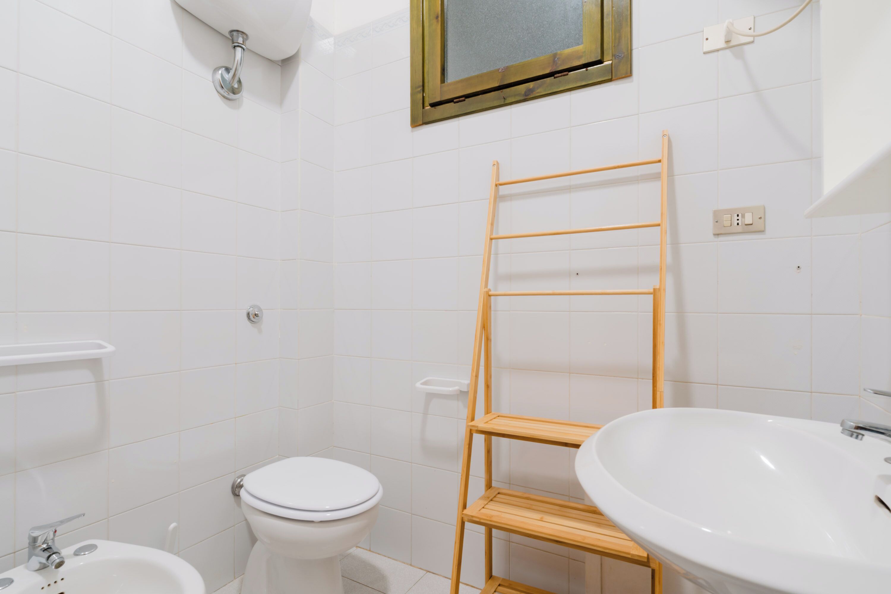 Een badkamer met toilet, bidet, wastafel en een houten plank.