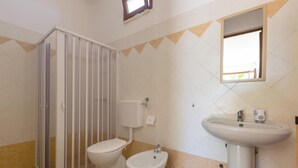 Une salle de bain comprenant un espace douche, des toilettes, un bidet, un lavabo et un miroir mural.