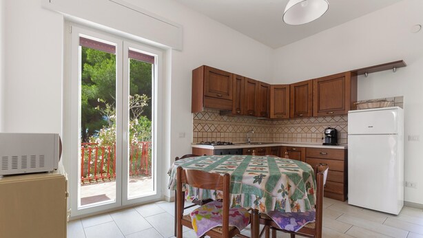 Une cuisine avec des meubles en bois, un réfrigérateur blanc et une table recouverte d’une nappe colorée.