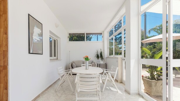 A bright, white interior with a round table and chairs, a potted plant, and a window with a view of greenery. - Villa Lina by BarbarHouse (Leporano)