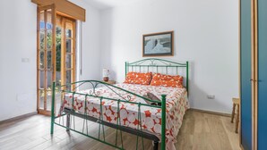 A bedroom with a green metal bed frame, a white and orange patterned bedspread, a framed picture on the wall, and a wooden door with a glass panel. - Villa Lina by BarbarHouse (Leporano)
