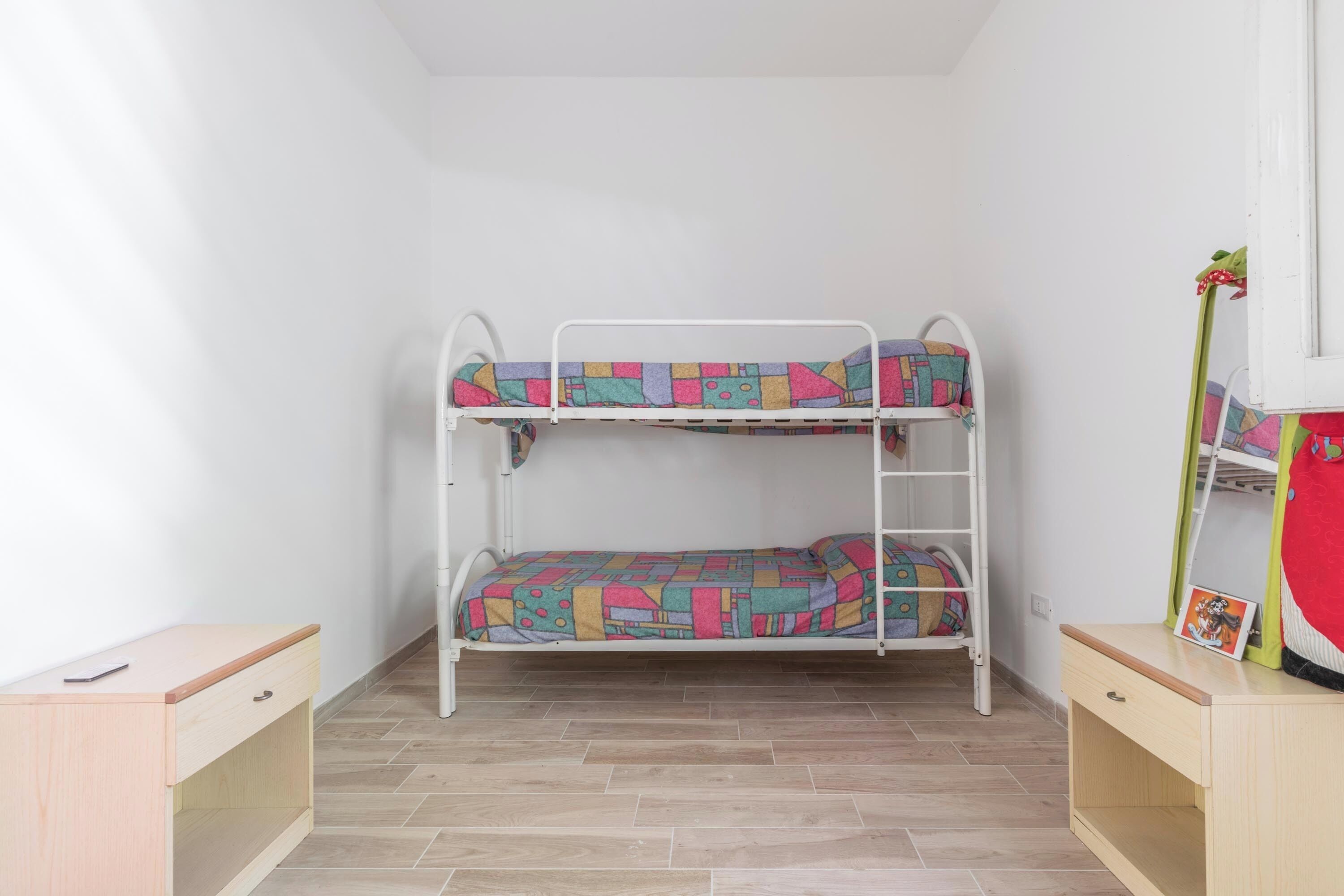 Un lit superposé avec une literie aux couleurs vives, un petit bureau et un miroir sur le côté droit.