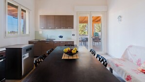 A modern kitchen with a dining area, featuring a large table, cabinets, and a view to an outdoor patio. - Villa Amelia by BarbarHouse (Torre Lapillo)
