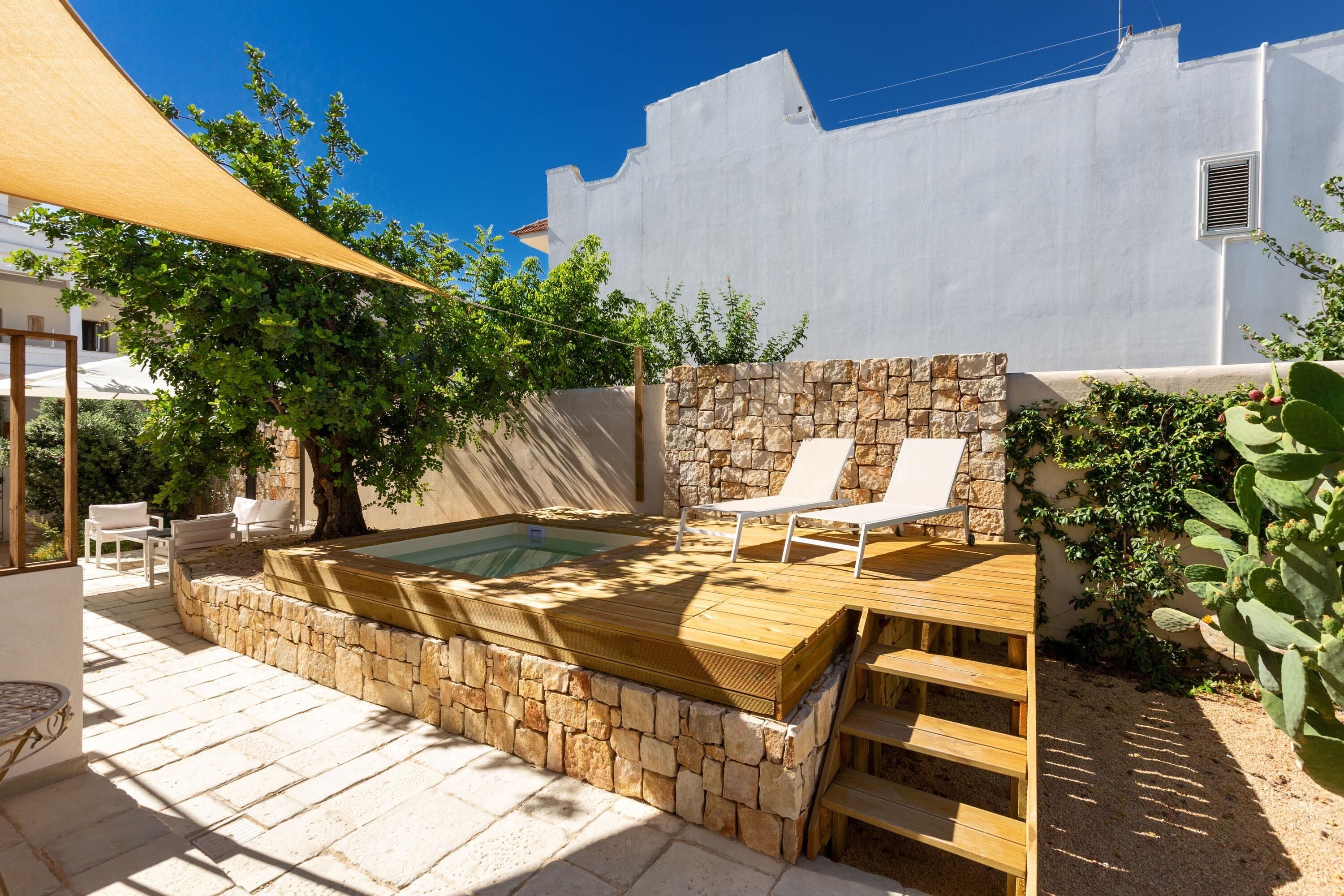 Un espace de bien-être comprenant un jacuzzi, une terrasse en bois, un mur en pierre et des murs blancs.