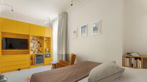 Une chambre à coucher avec un lit, une armoire jaune, une petite table, une chaise et une bibliothèque.