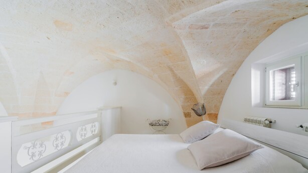 Una camera da letto con un letto bianco, un comodino e una finestra con vista sull'esterno.