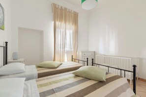 Un dormitorio con dos camas, una mesita de noche, un aparador y un ventanal con cortinas.