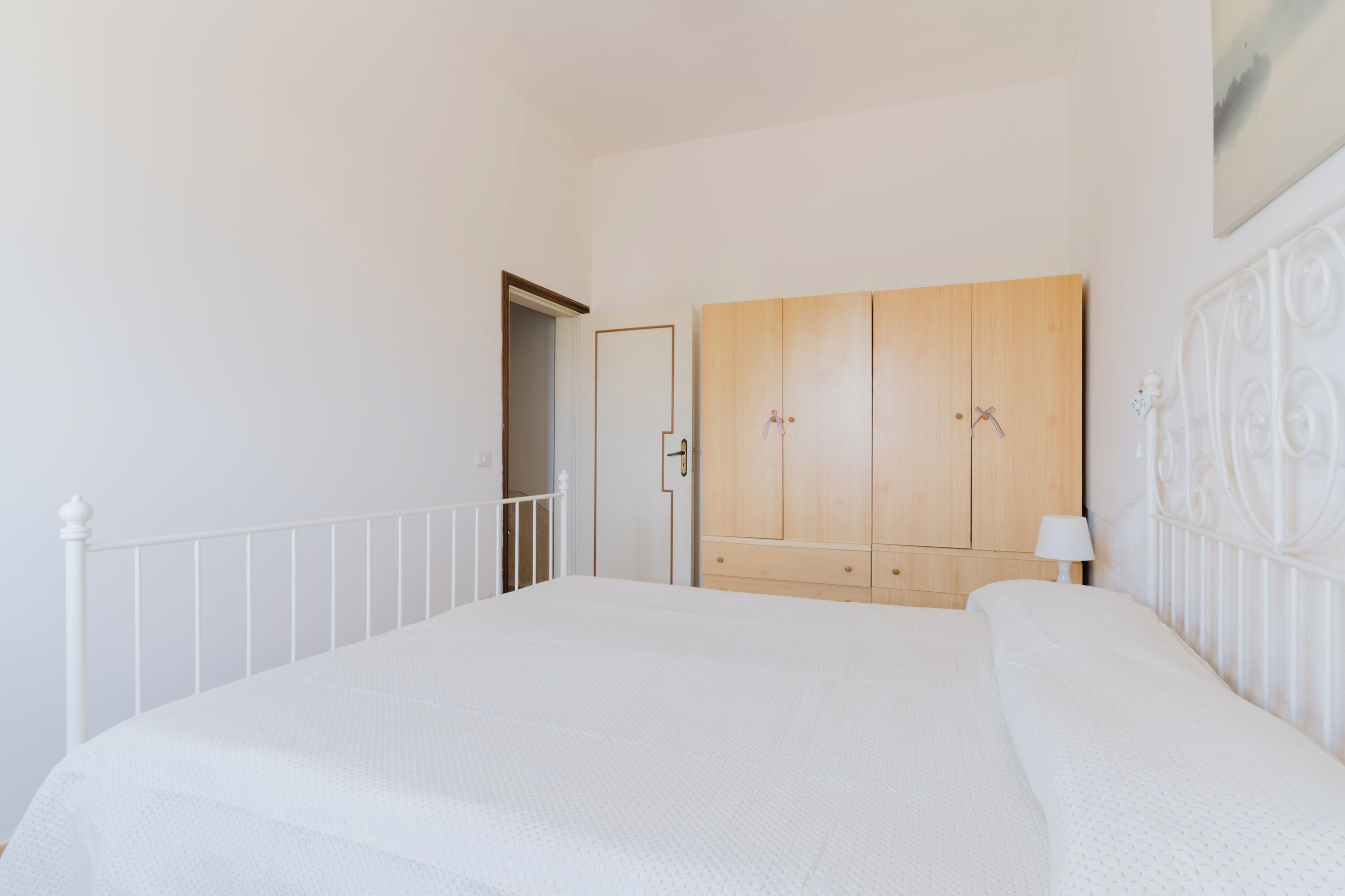 A bedroom with a large bed, a wardrobe, and a door leading to another room.