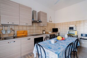 A modern kitchen with light wood cabinets, a stainless steel sink, a microwave, and a dining area with a table set for two. - Villetta Donna Mara by BarbarHouse (San Pietro in Bevagna)