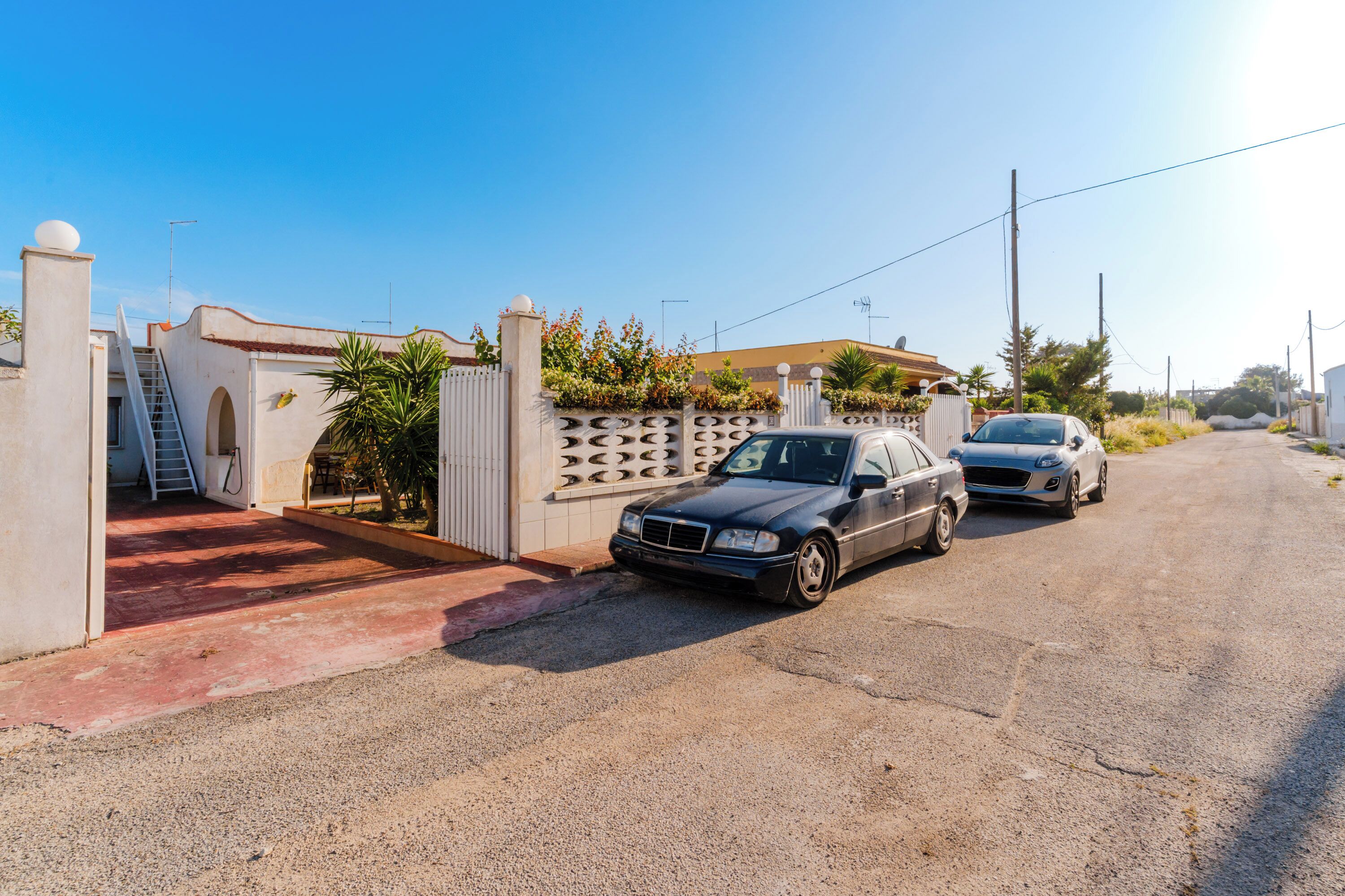 A street view with two parked cars, a gated entrance, and a clear sky.