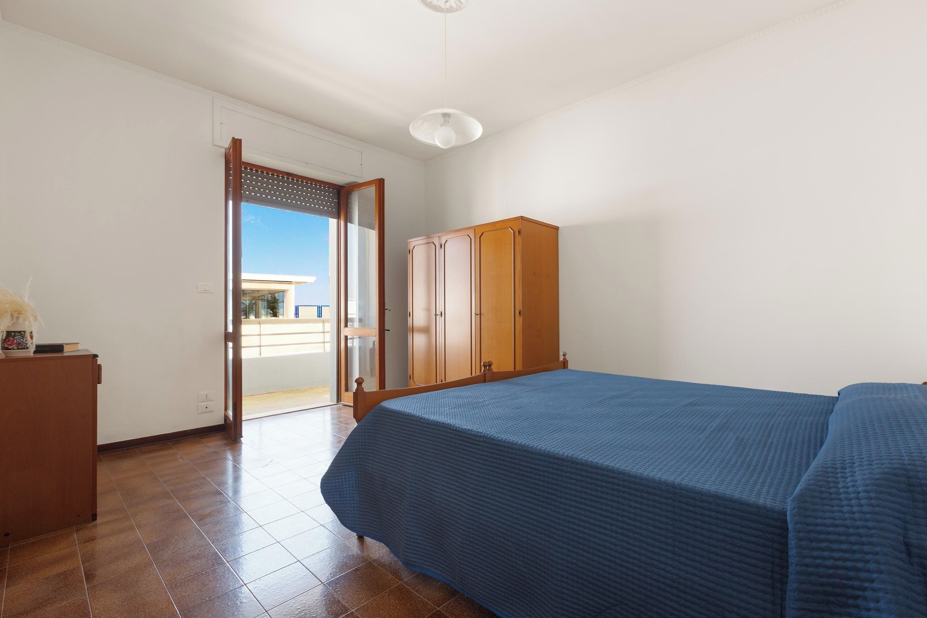 Une chambre à coucher avec un lit, une armoire en bois et une porte donnant sur un balcon.