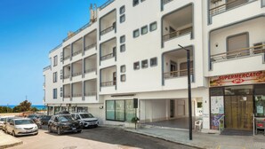 A multi-story building with a supermarket on the ground floor, several balconies, and parked cars in front. - Balconcino Vista Mare by BarbarHouse (San Foca)