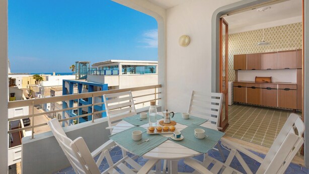 A balcony with a table set for breakfast, overlooking a coastal area with buildings and a clear sky. - Balconcino Vista Mare by BarbarHouse (San Foca)