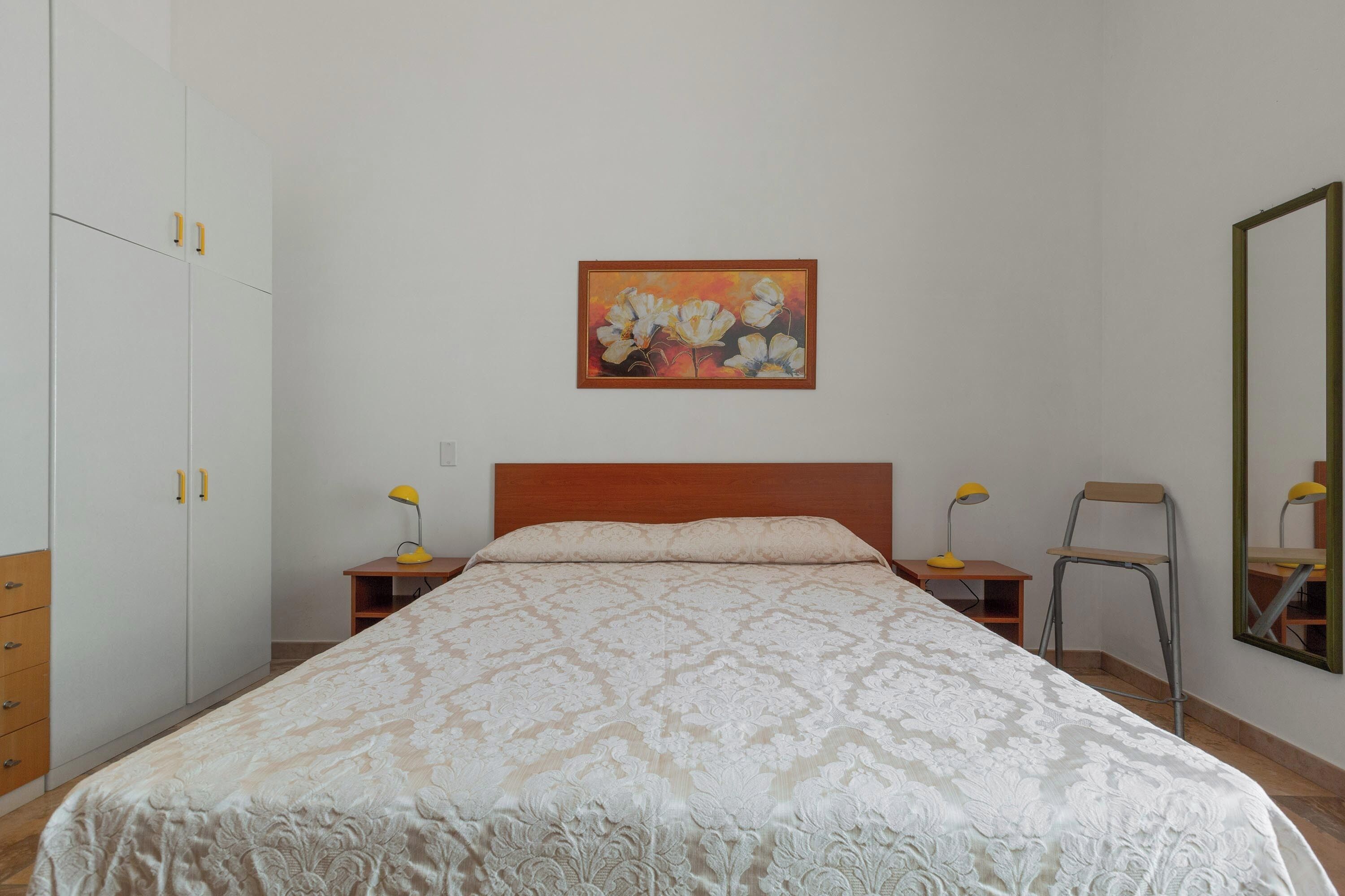A bedroom with a bed, a nightstand, a chair, a wardrobe, and a painting on the wall.