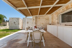 Eine Terrasse im Freien mit einer Steinwand, einer Holzbalkendecke und einem Esstisch für vier Personen.