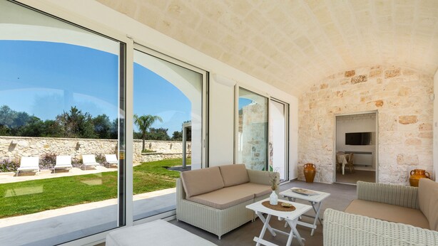 A modern outdoor living area with wicker furniture, large sliding glass doors, and a stone wall backdrop. - Trullo Pumo by Perle di Puglia (San Michele Salentino)
