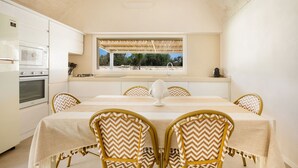 A dining area with a table set for four, surrounded by wicker chairs with a chevron pattern. A white vase is placed on the table. - Trullo Pumo by Perle di Puglia (San Michele Salentino)