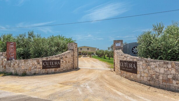 Een stenen muurpoort naar een landgoed genaamd 'Cultura Agri Resort', met een heldere lucht erboven.