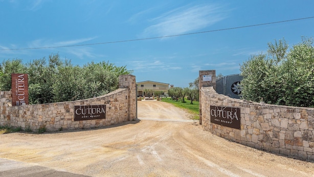 En stenvæg udgør indgangen til en ejendom kaldet 'Cultura Agri Resort' med en klar himmel over.
