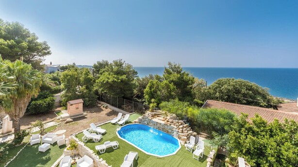 Una piscina rodeada de sillas de descanso blancas, un pequeño cobertizo y vistas al mar.