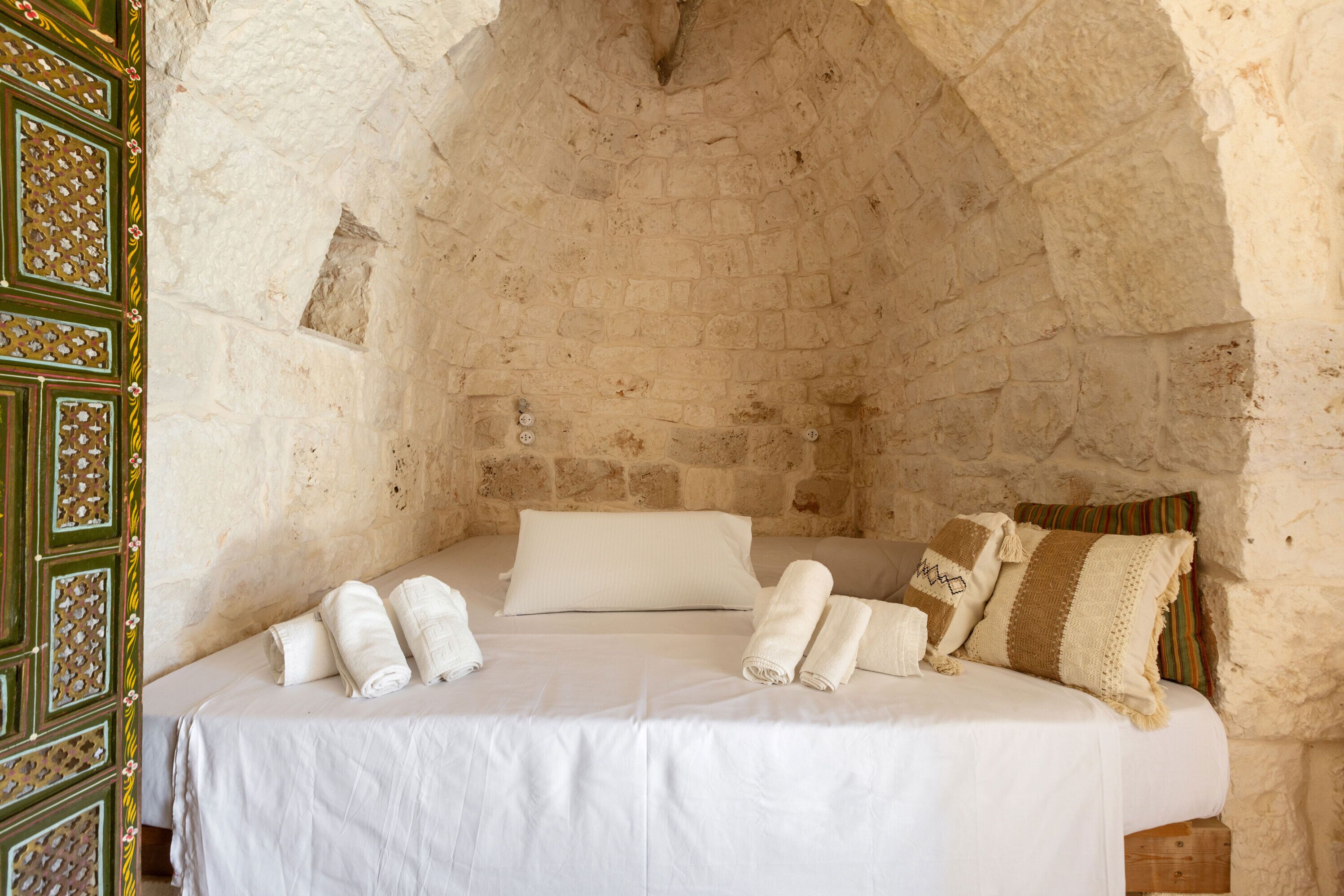 Une pièce aux murs de pierre, avec un lit, des oreillers et un panneau décoratif en bois.
