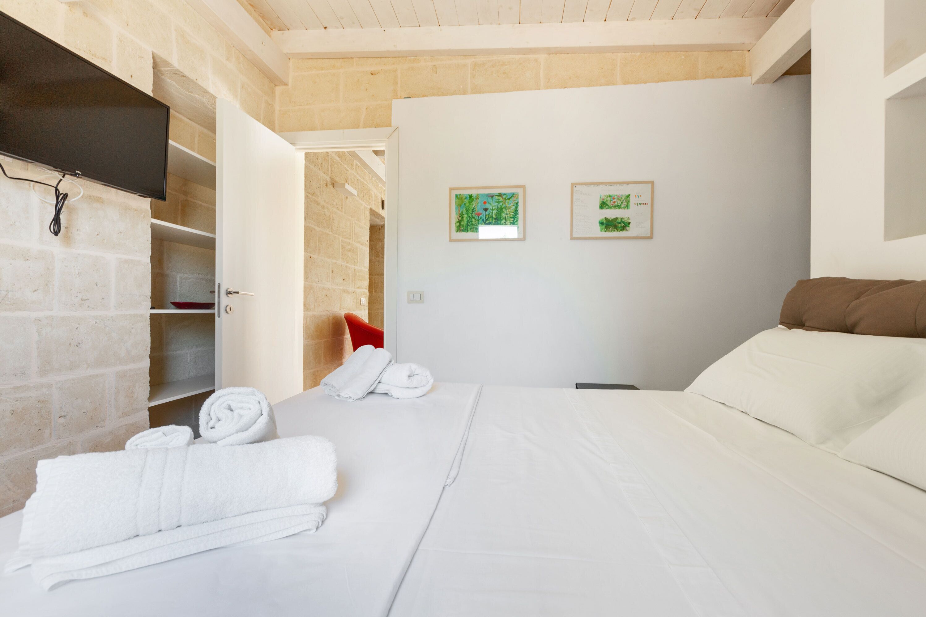 Een hotelkamer met een bed, witte handdoeken, een rode stoel en twee ingelijste foto's aan de muur.