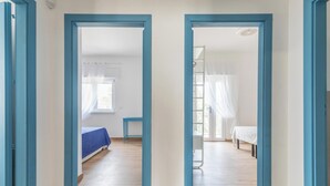 Un couloir avec deux portes ouvertes, dont l’une mène à une chambre à coucher équipée d’un lit et d’une table de chevet, et l’autre à une autre pièce comprenant un lit et une chaise.