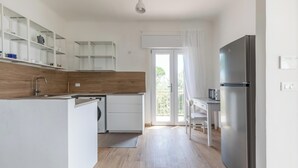 Une cuisine moderne avec des meubles blancs, un réfrigérateur en acier inoxydable et un coin repas comprenant une table et des chaises.