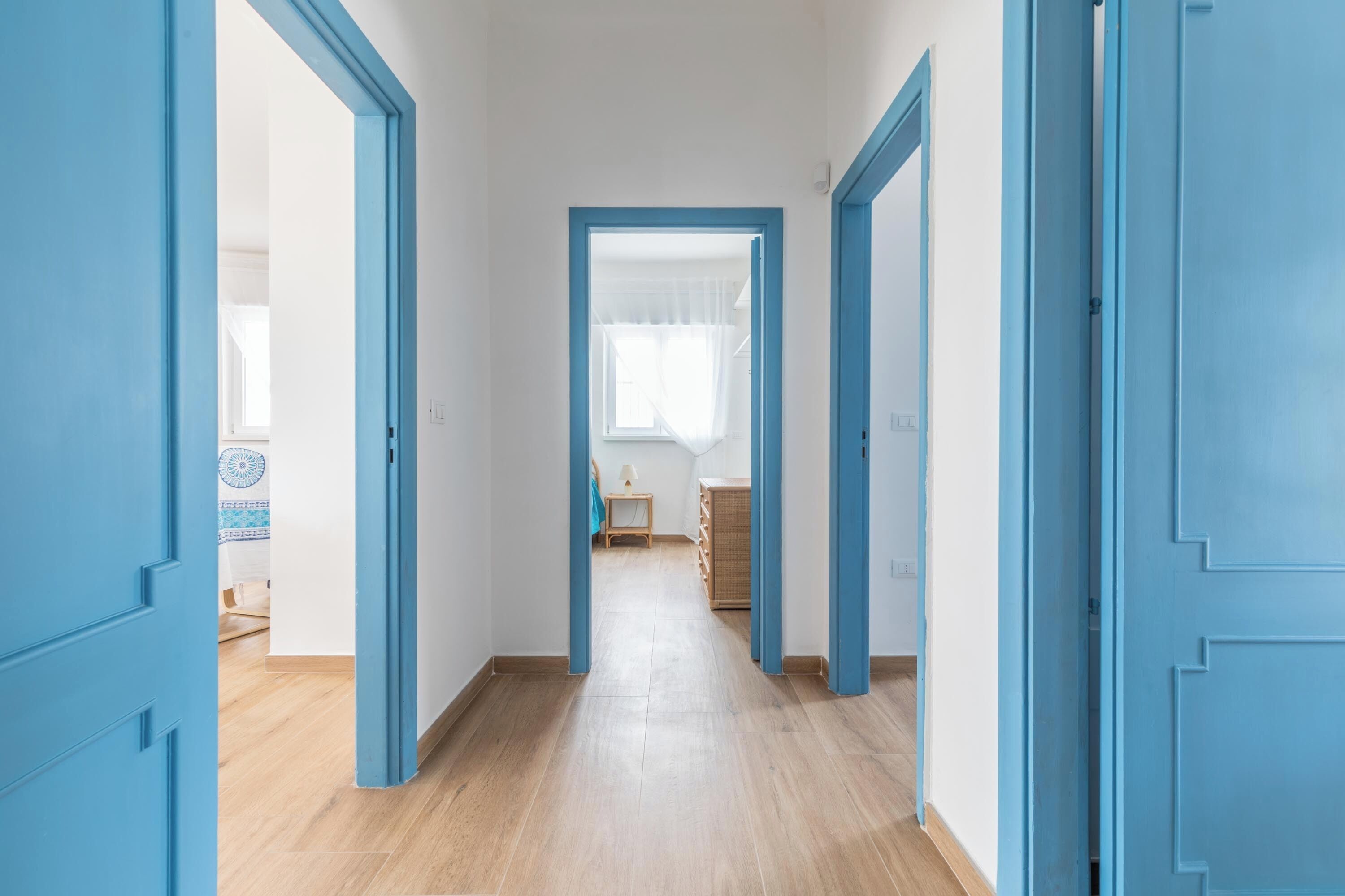 Een gang met blauwe deuren die leiden naar een kamer met een bed en een raam.