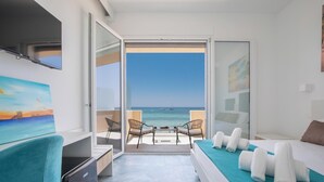 Een hotelkamer met een bed, een bureau, een stoel en een balkon met uitzicht op zee.