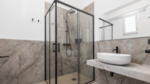 Un baño moderno con ducha envuelta en vidrio, lavabo blanco y paredes de mármol.