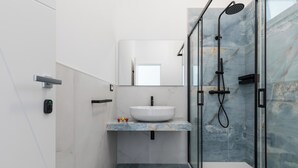 Een moderne badkamer met een witte wastafel, een marmeren aanrechtblad en een douchecabine met glazen wanden.