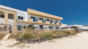 Een modern hotel met een plat dak, meerdere balkons en een zandstrand ervoor.