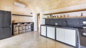 A kitchen with a brick ceiling, a black refrigerator, white cabinets, and a bar area with stools. - Villa Astra by Perle di Puglia (Ostuni)