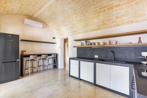 Eine Küche mit Backstein-Decke, einem schwarzen Kühlschrank, weißen Schränken und einer Bar mit Hockern.