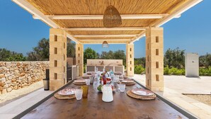 An outdoor dining area with a wooden table set for a meal, a stone wall, and a view of the sky. - Villa Astra by Perle di Puglia (Ostuni)