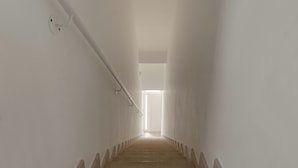 Ein schmaler, gut beleuchteter Gang mit einer Holztreppe zu einer hellen Tür.
