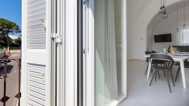 Ein stilvoller Essbereich mit weißem Tisch und Stühlen, einem Wand-Fernseher und einem Balkon mit Geländer.