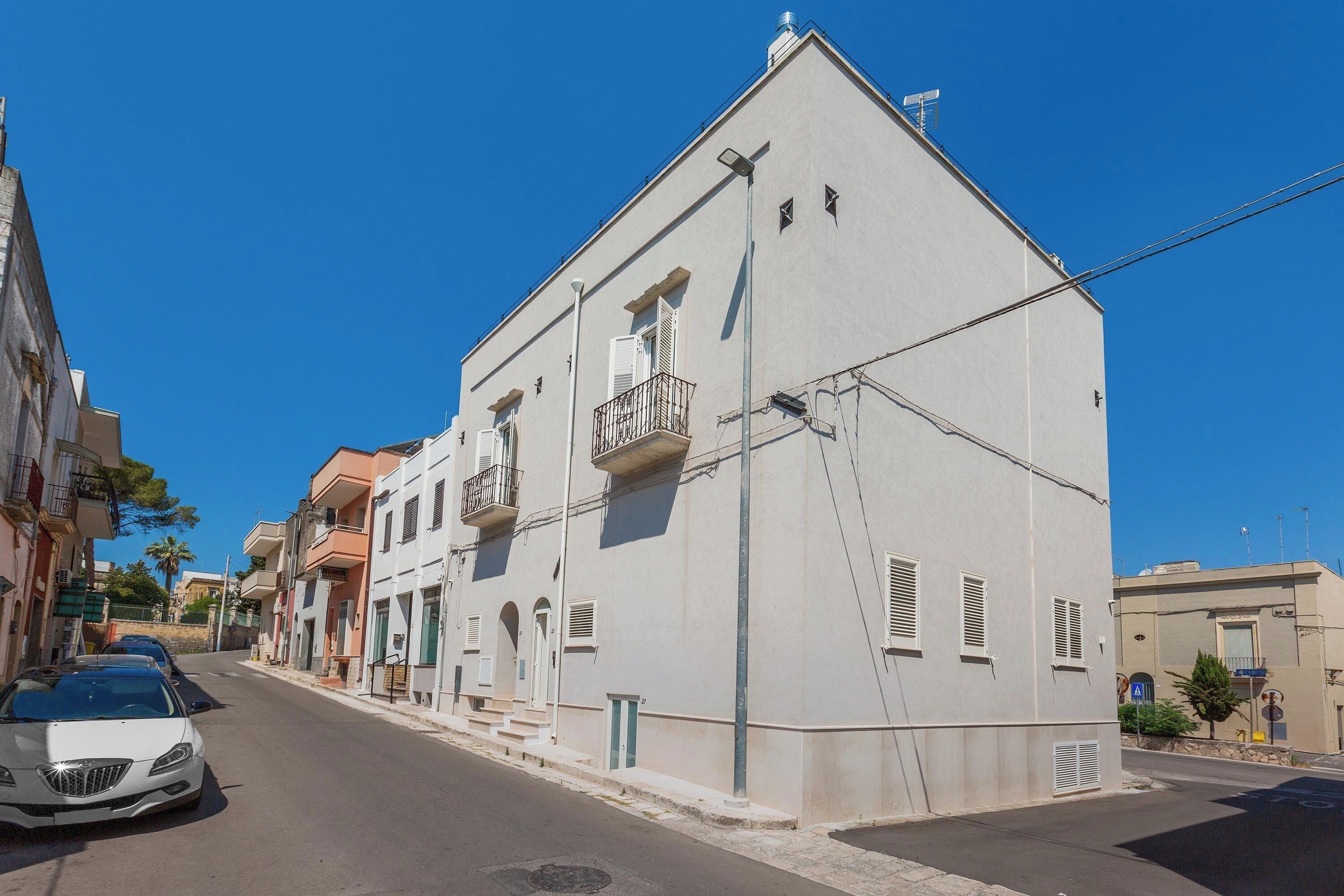 A street view with a white building, a parked car, and a clear blue sky.